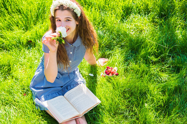 Girl reading a book on the green lawn in bright sunny day - 写真・画像