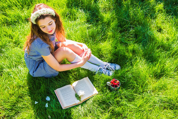 Tyttö lukee kirjaa vihreällä nurmikolla kirkkaana aurinkoisena päivänä
 - Valokuva, kuva