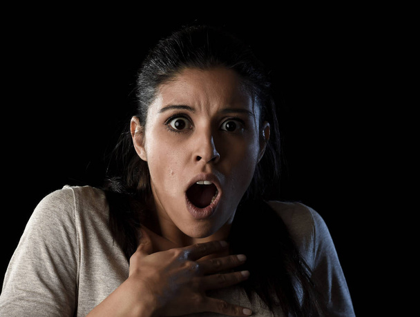 νεαρή όμορφη γυναίκα φοβάται Ισπανικά σε σοκ και έκπληξη έκφραση προσώπου που απομονώνονται σε μαύρο - Φωτογραφία, εικόνα