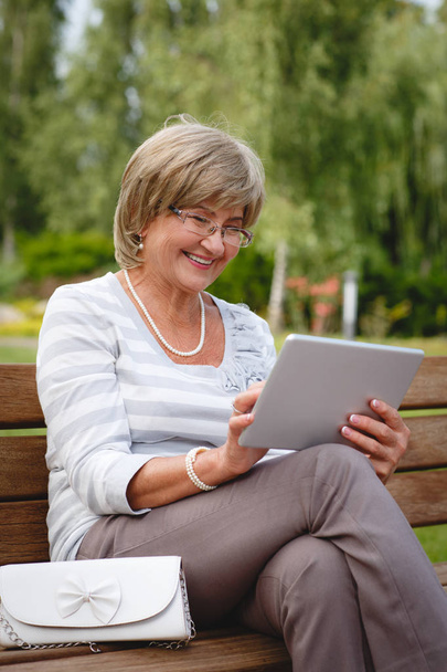 Привлекательная взрослая женщина с цифровым планшетом в парке
 - Фото, изображение