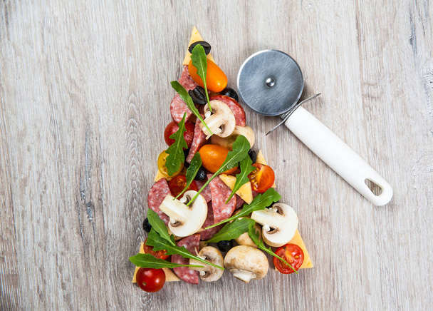 Creative composition of ingredients tomatoes, cheese, salami, mushrooms, arugula, olives in the form of a slice of pizza with pizza cutter - 写真・画像