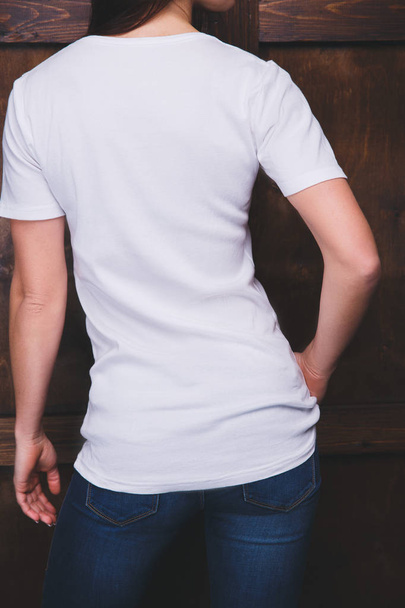 Woman wearing white t-shirt in front of wooden wall, back view - Foto, imagen