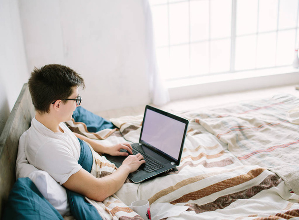 Casual jeune homme en utilisant un ordinateur portable dans le lit à la maison
 - Photo, image