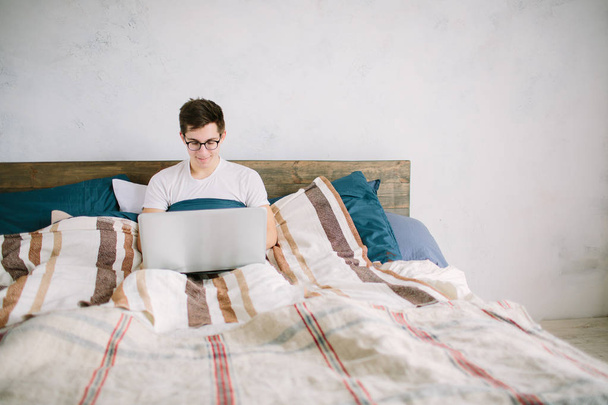 casual young man using laptop in bed at home - Foto, afbeelding