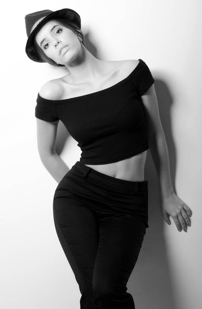 Piękna dziewczyna modne w czarne ubrania opierając się biała ściana - Zdjęcie, obraz