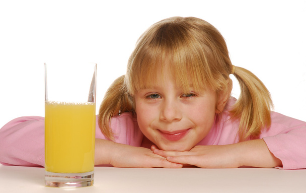 Little blonde girl behind an orange juice glass - Valokuva, kuva