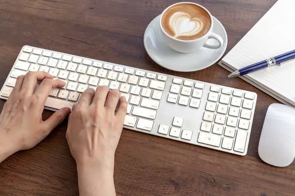 Typing and have a coffee cup of latte art heart shape on wooden  - Фото, изображение