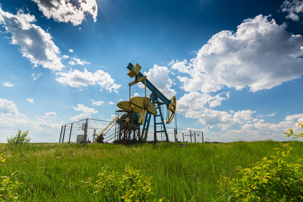 Operando poço de petróleo e gás no campo petrolífero europeu, perfilado no céu azul com nuvens cumulus, na primavera
 - Foto, Imagem