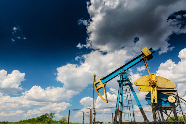 Эксплуатация нефтегазовой скважины на европейском нефтяном месторождении, профилированной на голубом небе с кучевыми облаками, весной
 - Фото, изображение
