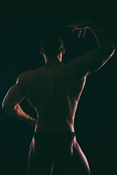 Silhouet van mooie bodybuilder op een donkere achtergrond. - Foto, afbeelding