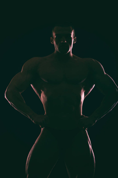 Σιλουέτα όμορφη bodybuilder σε σκούρο φόντο. - Φωτογραφία, εικόνα