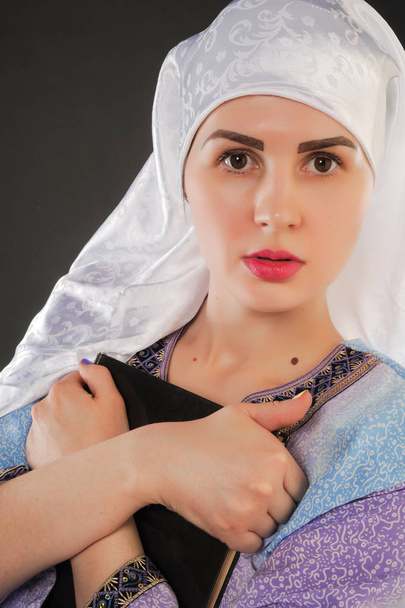 красивая девушка, мусульманка. в хиджабе. Изображение мусульманской девушки держит Коран. Вертикальный портрет красивой мусульманской девушки. В руках девушки Коран.
 - Фото, изображение