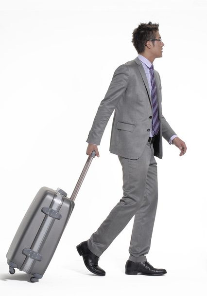 Young businessman walking and pulling his luggage. - Фото, изображение