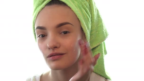young girl with towel on the hair causes a cream for the face and smiles - Felvétel, videó