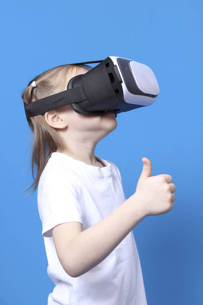 girl wearing virtual reality goggles and thumb up. isolated on blue background - Foto, Bild