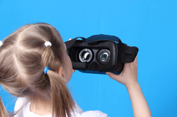 girl holding in the hands of virtual reality glasses. isolated on blue background - Photo, image