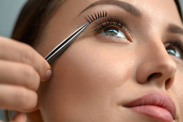 Beautiful Woman Applying Black Long Fake Eyelashes With Tweezers - Zdjęcie, obraz
