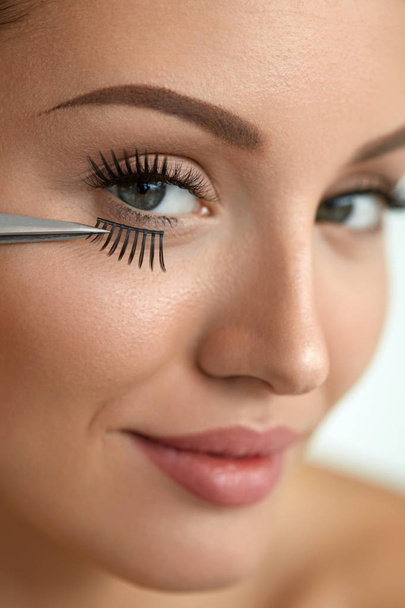Beautiful Woman Applying Black Long Fake Eyelashes With Tweezers - Фото, изображение