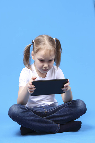 girl sits and plays on the tablet. isolated on blue background - Fotó, kép