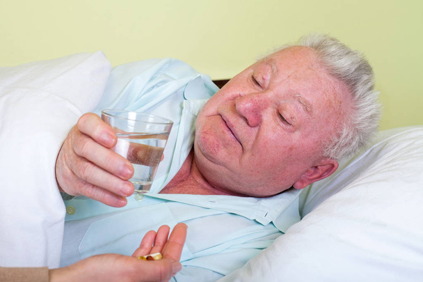 Sick old man in bed, receiving his pills - Foto, afbeelding