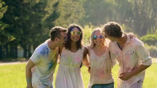 Groep vrienden bedekt met gekleurde verf dansende, juichende op buiten feest - Video