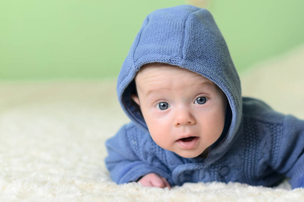 Μικρό αγόρι σε μπλε πλεκτή ζακέτα βρίσκεται στο στομάχι και να αναζητούν - Φωτογραφία, εικόνα