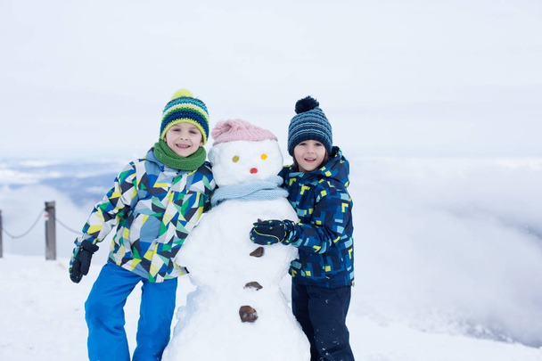 Two children, building snowman on top of mountain - Zdjęcie, obraz