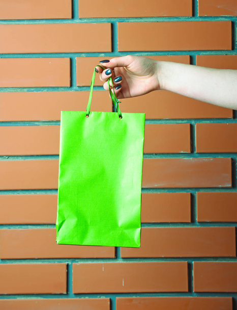 green shopping bag in female hand on brick wall - Photo, image
