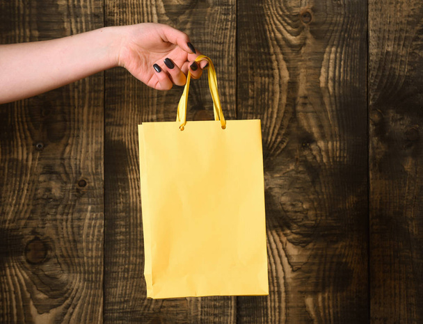 yellow shopping bag in female hand on wooden background - Zdjęcie, obraz