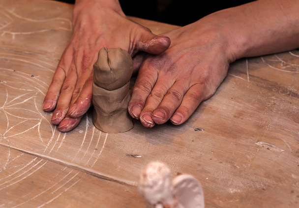 mãos que trabalham e escultura de acabamento com barro na mesa de madeira
  - Foto, Imagem