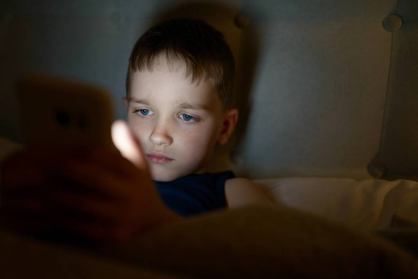 7 years old child boy using smartphone at night - Foto, Imagen