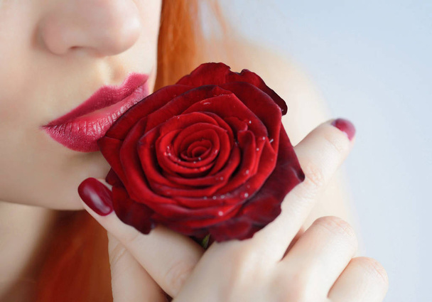 Ritratto con fiore di rosa rossa. Labbra e unghie rosso scuro. Bella giovane donna dai capelli rossi
. - Foto, immagini