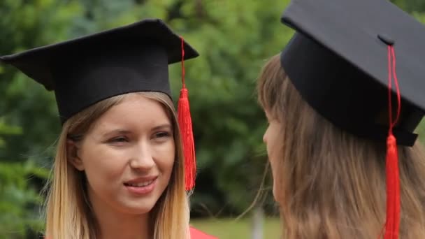 Dos mujeres jóvenes con gorras académicas con borlas comunicándose después de la graduación
 - Metraje, vídeo