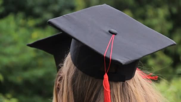 Dwóch studentów w graduation czapki z czerwona frędzle rozmawia w parku - Materiał filmowy, wideo