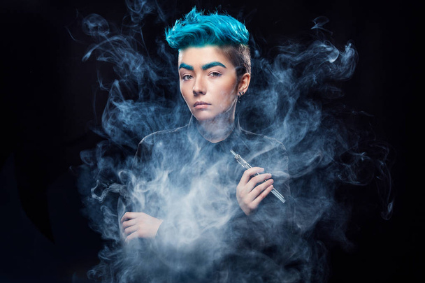 magic hipster woman with blue hair smoking vape on black background - Фото, изображение