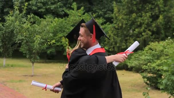 Glad woman and man in academic dresses embracing after graduation ceremony - Footage, Video