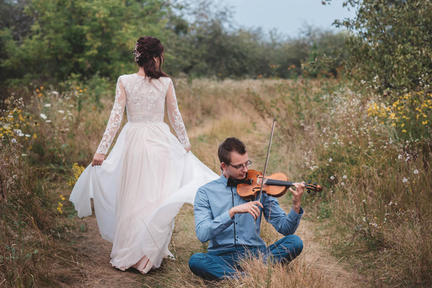 Violinist and woman in white dress , young man plays on the violin the background nature, - Photo, image
