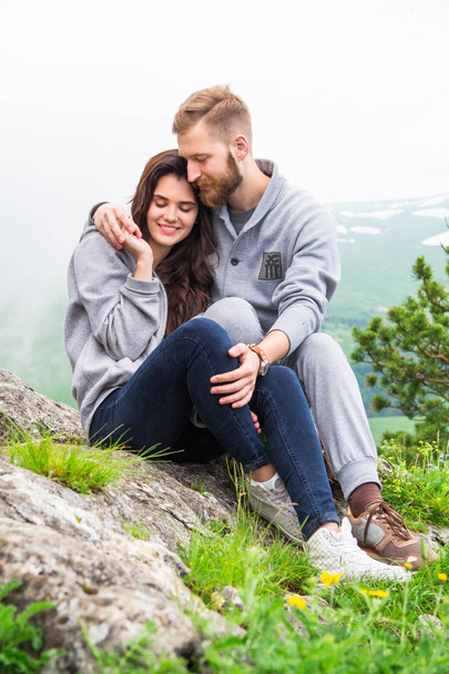 Счастливая молодая пара влюблена, сидя на горе, обнимаясь и вот
 - Фото, изображение