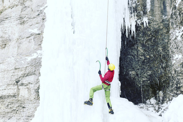 Ice climbing.Man climbing a frozen waterfall with ice tool. - Photo, image