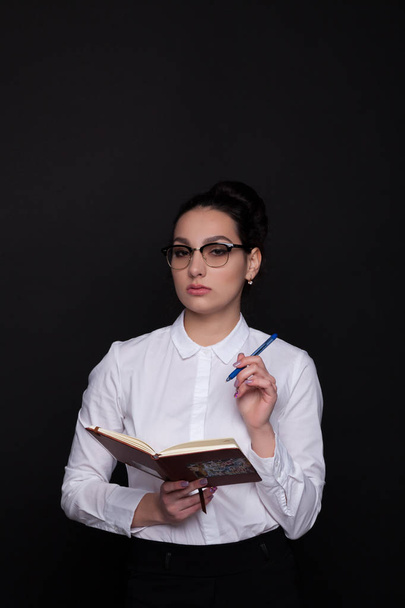 Mujer de negocios con un cuaderno y pluma en la mano sobre un fondo negro
 - Foto, Imagen