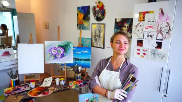 Beautiful Girl Artist Stands in Front of Camera With Arms Crossed in Front of Her and Holds in Hand Brush in Art Studio. - Footage, Video