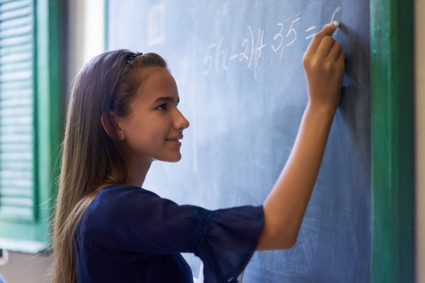 Κορίτσι κάνει άσκηση μαθηματικών στο μαυροπίνακα σε υψηλή σχολική τάξη - Φωτογραφία, εικόνα