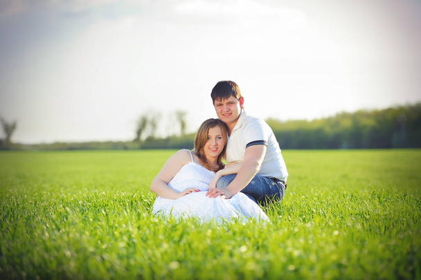 young pregnant couple sitting on green grass in spring  - Foto, Imagem