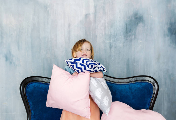 Le charmant porte-enfant sur le canapé avec des oreillers dans les mains
. - Photo, image