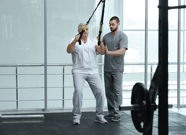 Rehabilitation concept. Mature man doing exercises under physiotherapist supervision - Photo, image