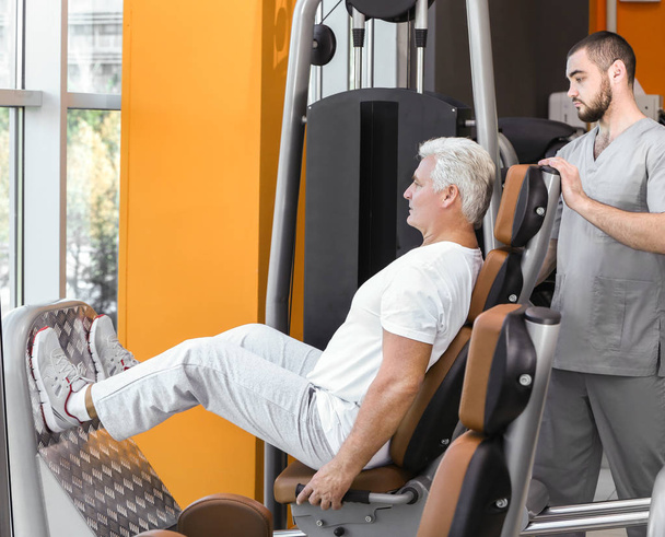 Rehabilitation concept. Mature man doing exercises under physiotherapist supervision - Valokuva, kuva