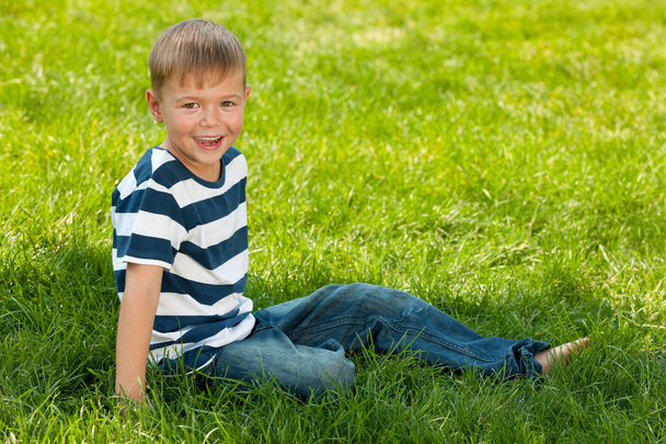 Sonriente chico se sienta en el parque de verano
 - Foto, Imagen