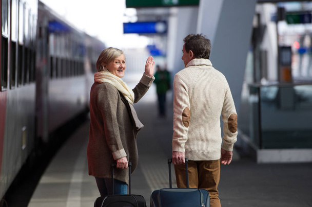 Senior couple on train station pulling trolley luggage. - 写真・画像