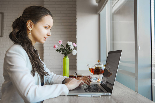 Dark-haired woman typing on laptop. Daylight from window illuminates table - Foto, immagini