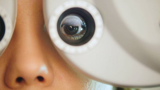 Mladá žena s červenými rty kontroluje oči na moderním zařízení v poliklinice, makro - Fotografie, Obrázek